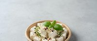 Fresh white cheese cubes with herbs and basil in wooden bowl on gray background for healthy cooking and Mediterranean cuisine recipes.