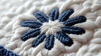Detailed macro shot of navy blue embroidered daisy flower on white fabric texture showing intricate needlework stitches and textile craftsmanship pattern.