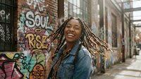 Young African American woman with dreadlocks laughing joyfully in urban alley with colorful graffiti street art background, expressing happiness and freedom.