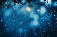 Magical winter night atmosphere with glowing bokeh lights and falling snow against dark blue background, creating dreamy festive mood.