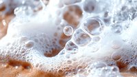 Macro shot of soap bubbles and foam creating abstract pattern with light refraction on orange background. Clean fresh texture with transparent spheres.