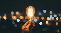 Hand holding glowing vintage Edison bulb against blurred city lights at night. Creative inspiration and innovation concept for business presentations.