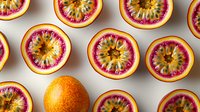 Fresh passion fruit halves arranged in rows showing vibrant pink and yellow pulp interior, with one whole orange fruit creating visual contrast on white background.