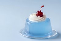 Blue jelly dessert topped with whipped cream and a red cherry on a light blue background, elegant sweet treat for food blogs.