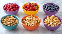 Fresh berries and crunchy granola in colorful ceramic bowls arranged on marble surface, healthy breakfast ingredients and nutritious snacks for balanced diet.