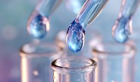 Liquid droplet falling from glass pipette into test tube, macro photography with soft purple and blue tones showing scientific research process.