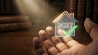 Businessman hand holding glowing house icon with 2027 year number and green upward arrow, symbolizing future property investment growth and real estate market success.