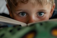 Young blonde boy with blue eyes reading book, close-up portrait showing curiosity and learning. Educational concept for children literacy and development.