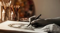 Artist hand sketching portrait drawing with pencil in creative studio workspace with art supplies and paintbrushes in background for artistic projects.