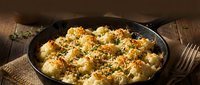 Creamy baked cauliflower gratin with golden breadcrumb topping in cast iron skillet on rustic wooden table for comfort food recipes and cooking blogs.