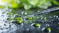 Macro shot of glass dropper with green liquid essence and water drops on dark surface against blurred natural background. Wellness and aromatherapy concept.