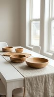 Wooden bowls arranged on linen table runner in bright dining room with natural light from windows creating minimalist Scandinavian kitchen decor.