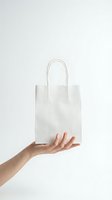 Hand holding white paper shopping bag on neutral background for retail and commercial use.