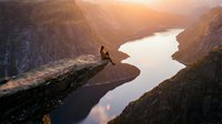 Hiker silhouette on cliff edge overlooking fjord at golden hour sunrise. Adventure travel concept for outdoor recreation and mountain hiking destinations.