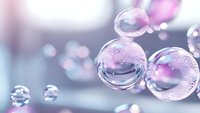 Transparent water drops with pink and purple bokeh background create dreamy macro photography effect. Spherical bubbles show surface tension and reflection.