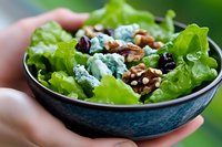 Fresh green salad with blue cheese crumbles, crunchy walnuts and dried cranberries served in dark ceramic bowl, close up view. Perfect for food blogs and menus.
