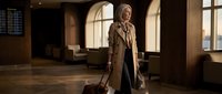 Professional businesswoman with luggage walking through modern airport terminal during golden hour travel concept.