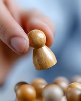 Wooden pawn figure held between fingers against blurred background, showing leadership concept and strategic business decision making in board games.