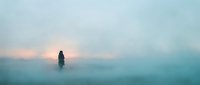 Woman standing alone in dense fog at sunrise, silhouetted against misty landscape. Suitable for concepts of solitude, contemplation, and atmospheric moods.