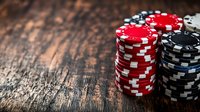 Stacked red and black poker chips on rustic wooden table with dramatic lighting and shallow depth of field, creating atmospheric casino gaming ambiance.
