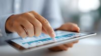 Close up view of business person analyzing financial statistics on digital tablet screen, finger touching graph data on modern device display.