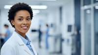 Confident African American female doctor smiling in modern hospital corridor wearing white medical coat for healthcare and medical profession concepts.