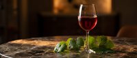 Elegant red wine glass with fresh grape leaves on rustic wooden table in warm candlelit atmosphere for dining and hospitality concepts.
