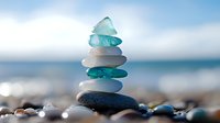 Balanced stack of sea glass and smooth stones on beach shoreline creating zen-like harmony against blurred ocean background.