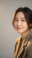Professional Asian businesswoman with warm smile wearing brown blazer against neutral background for corporate headshot and business portrait.