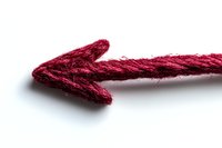 Red rope twisted into arrow shape pointing left on white background, macro view showing textile texture and fibers. Isolated design element.