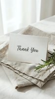 Thank you card with cursive script resting on folded linen fabric beside a fresh rosemary sprig, soft natural light, minimal style.