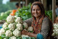 Smiling South Asian woman vendor selling fresh cauliflower at local farmers market, showcasing organic produce for healthy cooking.