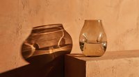 Two glass vases with organic shapes casting warm shadows on terracotta wall. Minimalist still life arrangement suitable for home decor, interior design, and lifestyle publications.