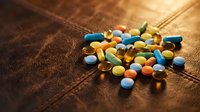 Colorful pharmaceutical pills and capsules scattered on wooden surface with warm lighting for medical and healthcare concepts.
