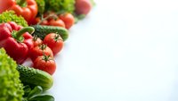 Fresh organic vegetables including red bell peppers, tomatoes, broccoli and leafy greens arranged on white background with copy space for healthy eating concepts.