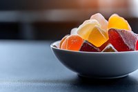 Colorful fruit jelly candies in white ceramic bowl on dark background. Sweet gummy dessert with various flavors and shapes for confectionery design.
