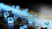 Fiber optic cables with glowing blue light streams connecting to computer circuit board with microchips and electronic components for data transmission technology.