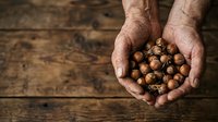 Farmer's hands holding freshly harvested hazelnuts over rustic wooden surface, showcasing organic nut farming and harvest season.