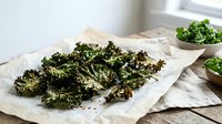 Crispy baked kale chips seasoned with sea salt on parchment paper, healthy snack alternative for clean eating and nutritious diet lifestyle.