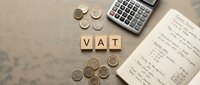 VAT tax calculation concept with wooden letter blocks, calculator, coins and financial notes on neutral background for accounting services.
