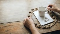 Hands holding warm coffee mug on wooden tray with cozy blanket, creating peaceful morning atmosphere on rustic table for relaxation and comfort lifestyle.