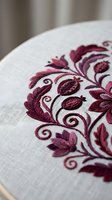 Elegant burgundy floral embroidery on white linen fabric showcasing intricate needlework with decorative swirls and leaves for luxury textile design projects.