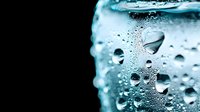 Macro shot of water droplets and condensation on cold glass surface with turquoise blue tint, showing refreshing bubbles and moisture patterns in extreme detail.