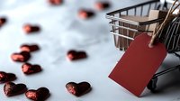 Shopping cart with red blank tag and scattered glittery heart shaped decorations on light background, romantic shopping concept for Valentine's day.