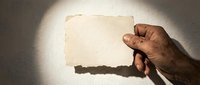 Hand holding blank vintage paper card with torn edges against textured wall background for mockup design projects and creative presentations.
