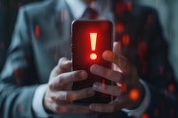 Businessman holding smartphone with glowing red exclamation mark warning sign, concept of cyber security threat, data breach or mobile device alert for business risk management.
