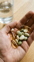Hand holding assorted nutritional supplements and vitamins including capsules and tablets with glass of water on wooden surface for wellness and health.