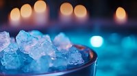 Crushed ice cubes in glass with glowing candlelight bokeh creating atmospheric mood. Blue and orange tones blend for relaxing spa or cocktail ambiance.