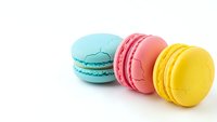 Colorful French macarons in mint green, pink and yellow arranged in row on white background for bakery menu design and confectionery advertising.