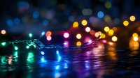 Colorful LED string lights with bokeh effect creating festive atmosphere on dark surface. Multi-colored illumination for holiday decorations and celebrations.